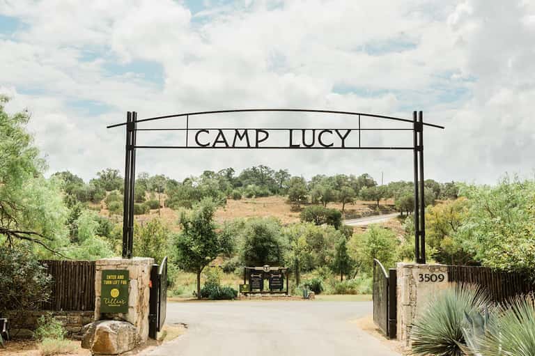 Camp Lucy entrance gate with rustic metal arch and pastoral landscape view