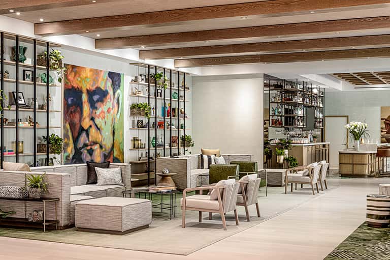 Modern hotel lobby with exposed wood beams, shelving displays, contemporary furniture, and colorful abstract artwork
