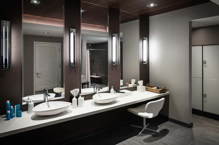 Luxury bathroom with dual vanities, large mirrors, illuminated sconces, and dark wood accent walls