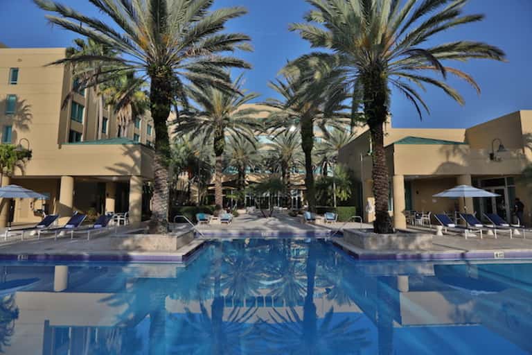Resort pool courtyard surrounded by palm trees and cream-colored hotel buildings
