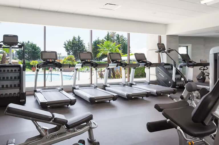 Modern fitness center with cardio equipment and large windows overlooking outdoor pool and landscaping