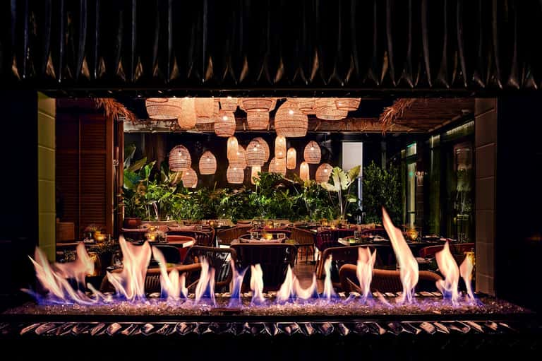 Elegant outdoor dining area with fire pit, hanging lanterns, and lush greenery at night