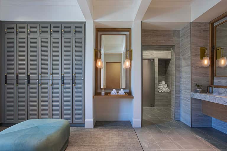 Luxury spa locker room with wooden lockers, vanity mirrors, pendant lighting, and access to shower area