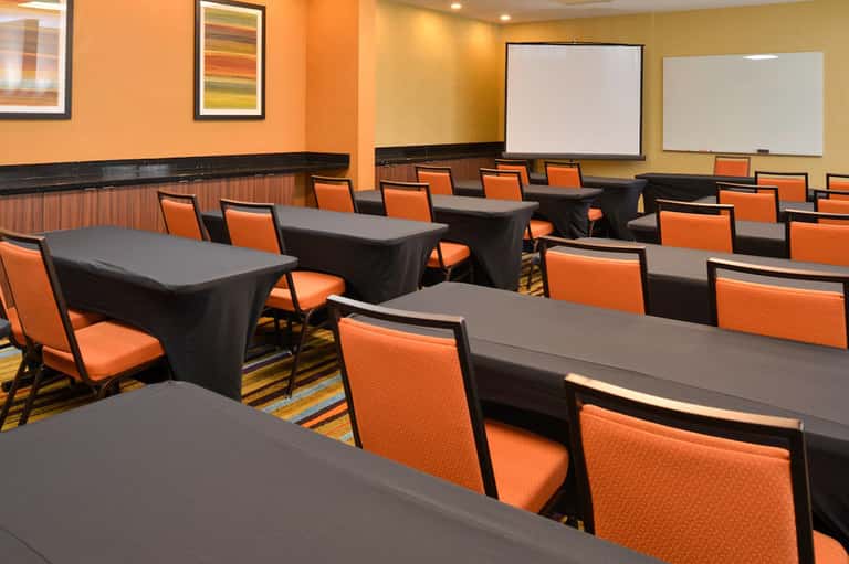 Modern conference room with orange chairs, black tables with black table skirts, and presentation screens on walls