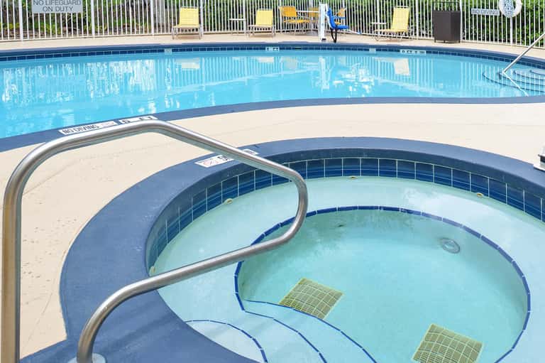 Resort swimming pool with spa tub, lounge chairs, and white fencing under clear sky