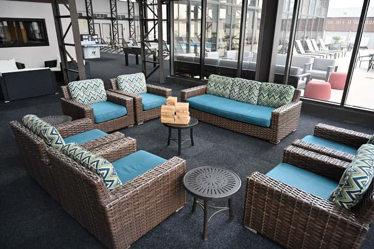 Indoor lounge area with wicker furniture, blue cushions, and geometric patterned pillows arranged around small tables