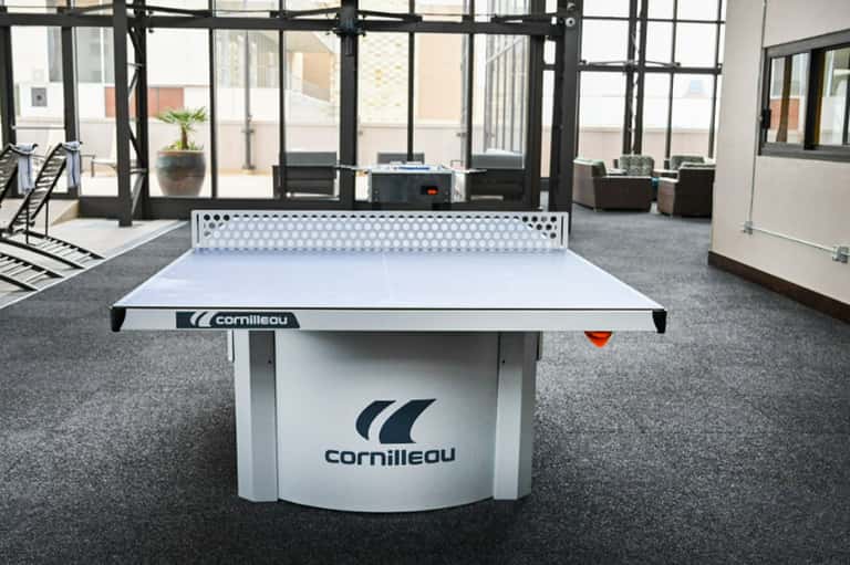 Cornilleau white ping pong table in modern indoor recreation room with floor-to-ceiling windows
