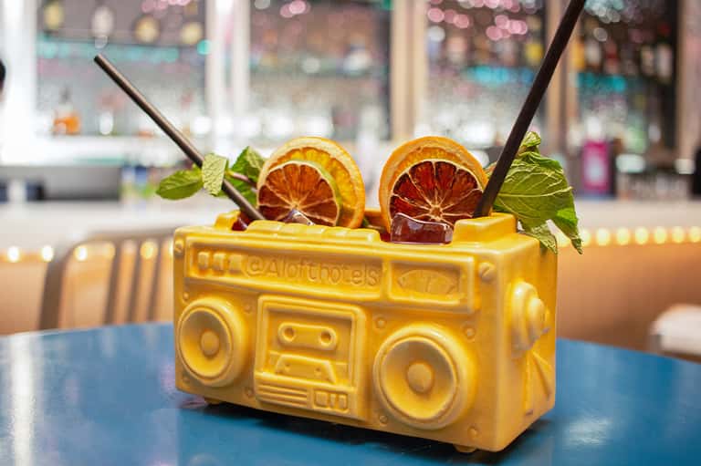 Yellow boombox-shaped cocktail glass with orange citrus slices and mint garnish on blue table