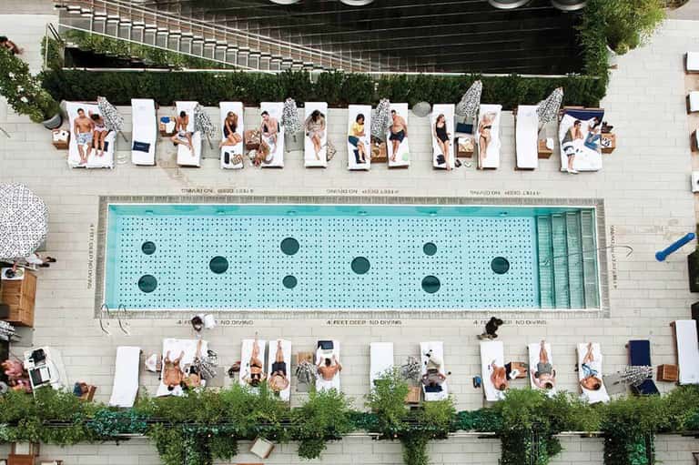 Aerial view of resort pool with swimmers on lounge chairs along the deck and green landscaping