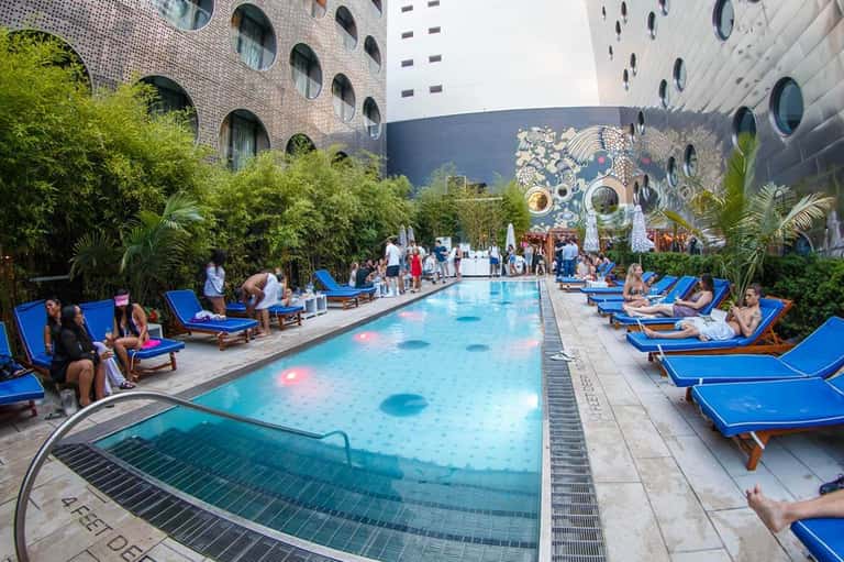 Courtyard pool with blue lounge chairs, palm trees, and modern high-rise buildings with circular windows