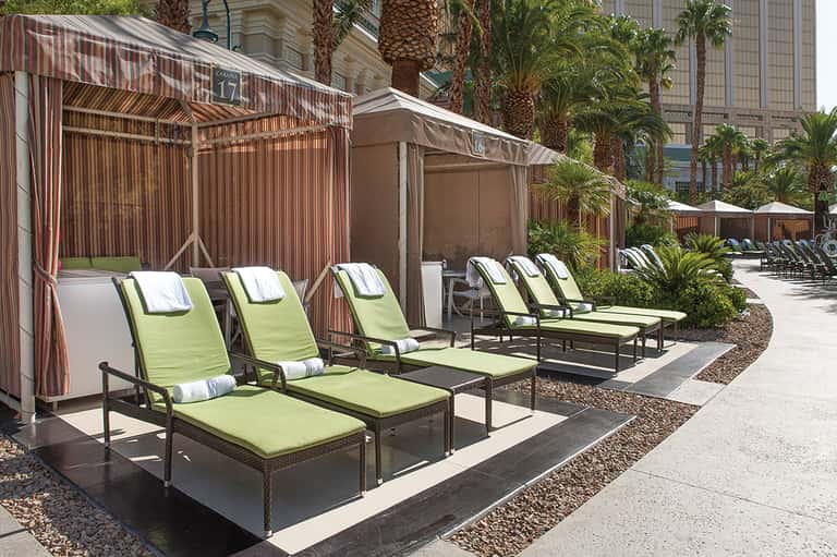 Outdoor lounge area with lime-green chaise lounges under striped cabanas and palm trees
