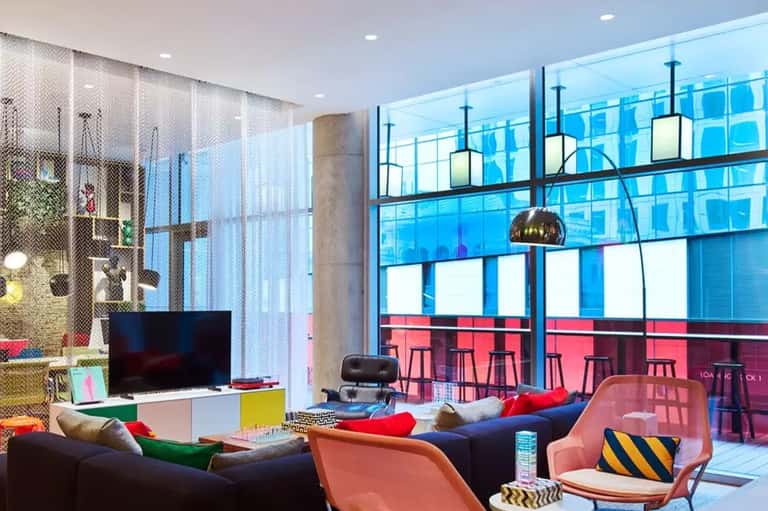 Modern hotel lounge with colorful furniture, floor-to-ceiling windows, and city skyline views