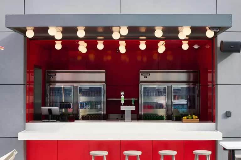 Modern red food kiosk with illuminated counter, refrigerated cases, and white seating stools