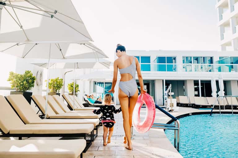 Woman and child walking toward pool area with white umbrellas and loungers at modern resort