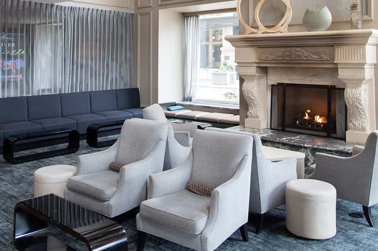 Elegant living room with navy sectional sofa, fireplace with stone mantel, and floor-to-ceiling windows with sheer curtains