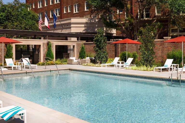 Resort outdoor pool with lounge chairs, red umbrellas, and brick building facade with ivy