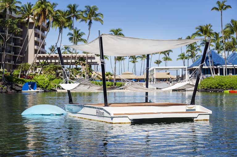 Luxury floating cabanas with canopy on calm water surrounded by palm trees and resort buildings