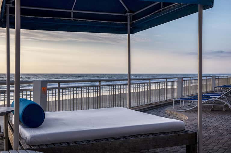 Oceanfront cabana bed with blue canopy on beach deck overlooking calm turquoise waters