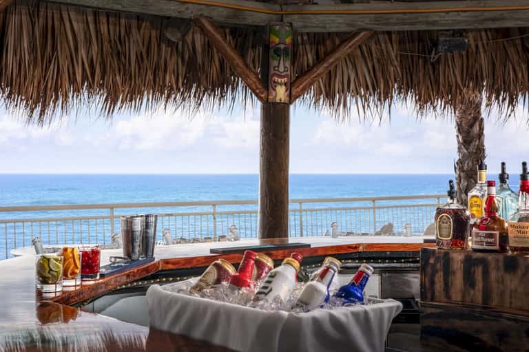 Beachfront tiki bar with ocean view, tropical thatch roof, and ice bucket with assorted beverages