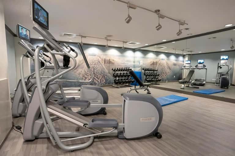 Modern fitness center with cardio equipment, dumbbells, blue exercise mats, and motivational wall mural