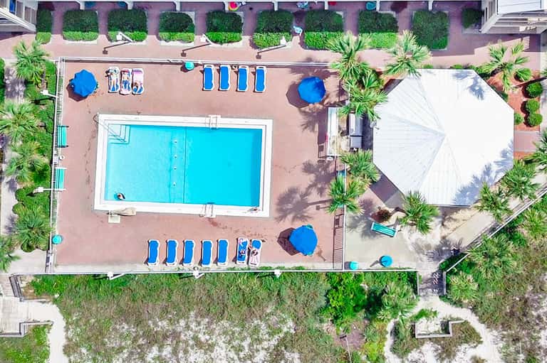 Overhead view of resort pool deck with loungers, umbrellas, and palm trees