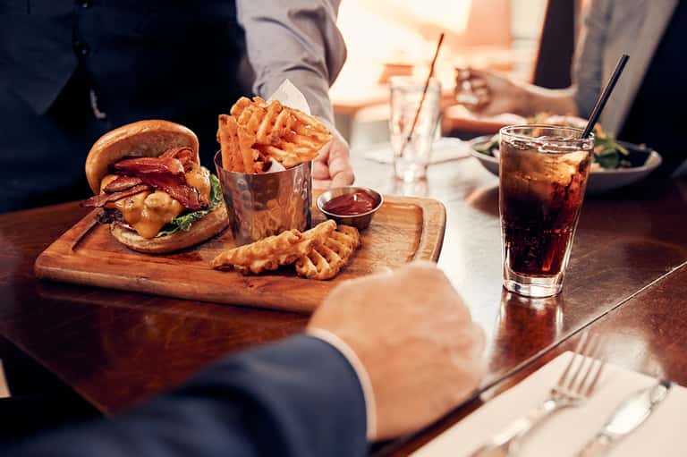 Business lunch with gourmet burger, waffle fries, and cola at restaurant table