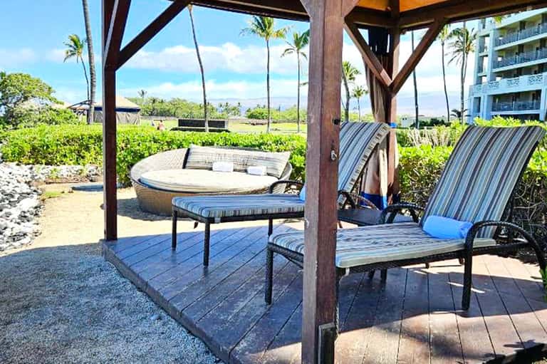 Beach cabana area with lounge chairs and fire pit overlooking ocean and palm trees