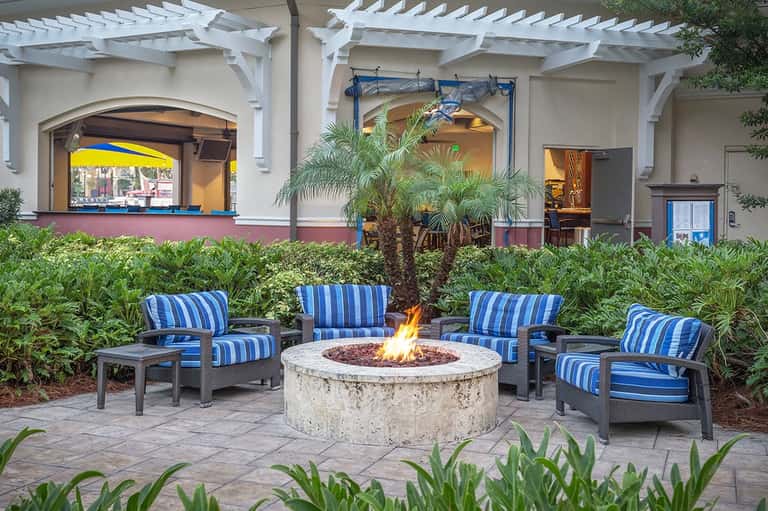 Outdoor fire pit lounge area with blue striped chairs surrounded by tropical landscaping