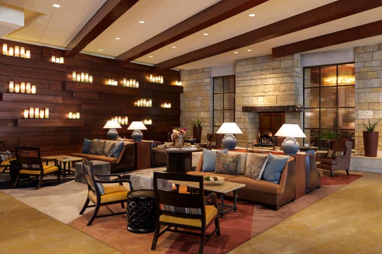 Elegant hotel lobby with dark wood accents, fireplace, brown leather seating, and decorative candle wall lighting