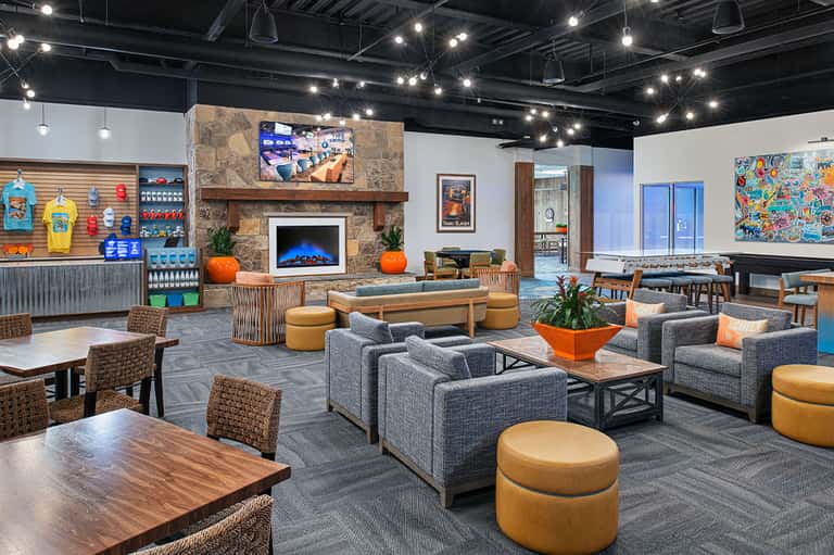Modern hotel lounge with gray seating, fireplace, stone accent wall, and colorful artwork on exposed beam ceiling