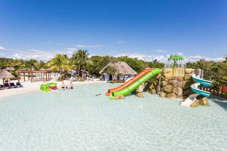 Shallow lagoon-style pool with colorful water slides and rock formations, palm trees in background