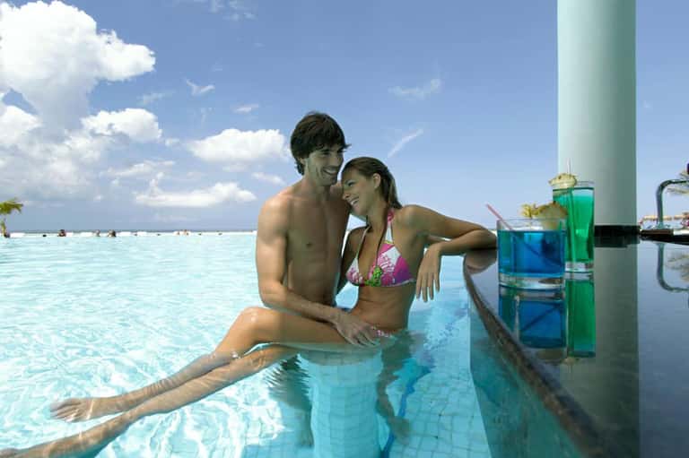 Couple relaxing in tropical infinity pool with colorful cocktails and ocean view