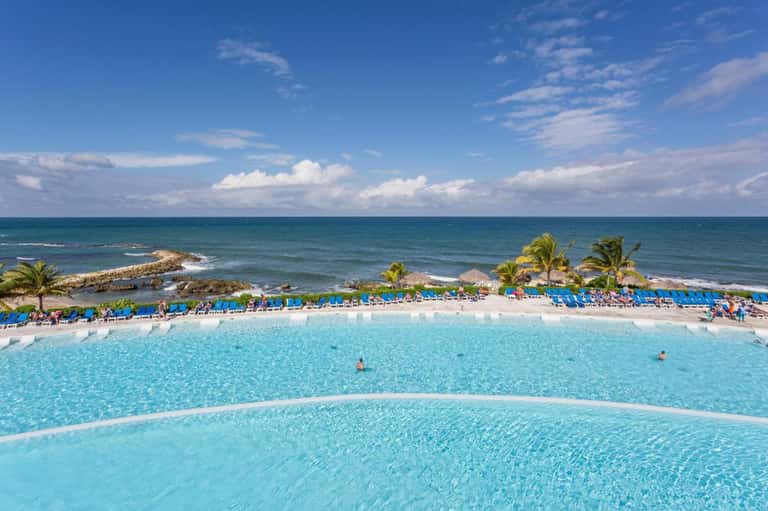 Resort pool with turquoise water, lounge chairs, palm trees, and ocean view in background
