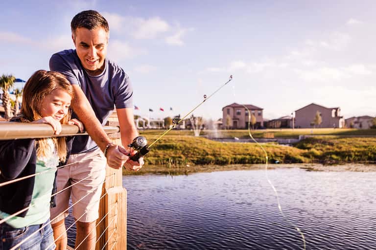 Adult and child fishing together from a wooden dock overlooking a residential community and waterway