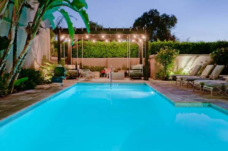 Backyard swimming pool with lit pergola, lounge chairs, and lush green landscaping