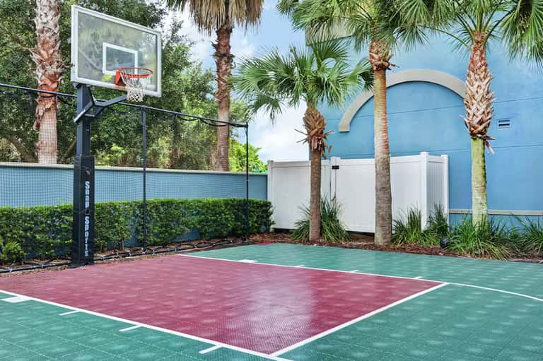Outdoor basketball court with colorful sport surface surrounded by palm trees and blue building