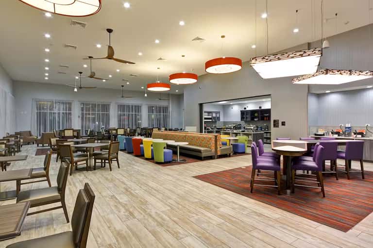 Modern resort dining and lounge area with colorful seating, orange pendant lights, and floor-to-ceiling windows