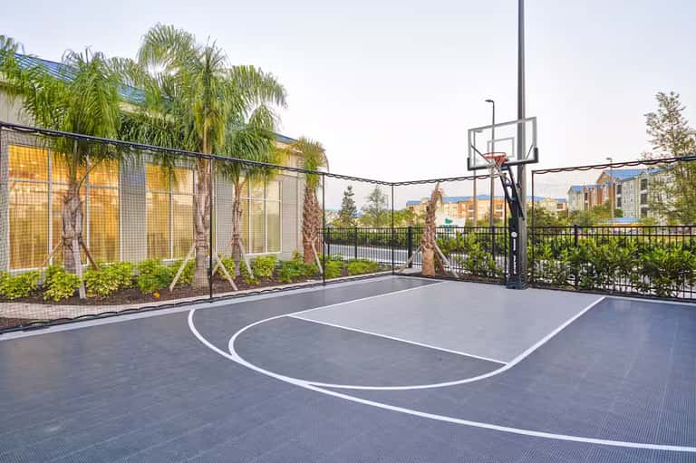 Outdoor basketball court with palm trees, yellow building, and black metal railings overlooking residential area