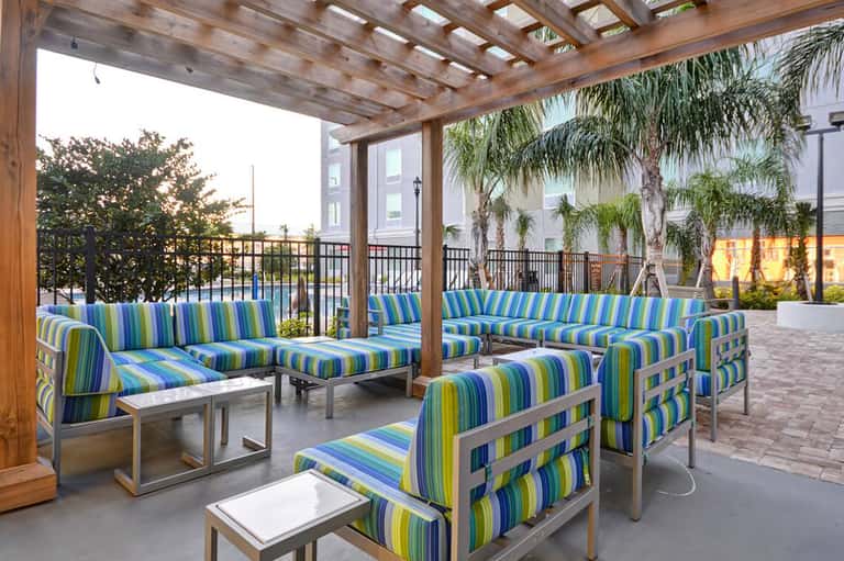 Covered terrace with striped blue and green lounge chairs, wooden pergola, and palm trees in background