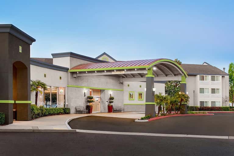 Modern hotel exterior with lime green accents, curved architectural features, and palm trees in landscaping