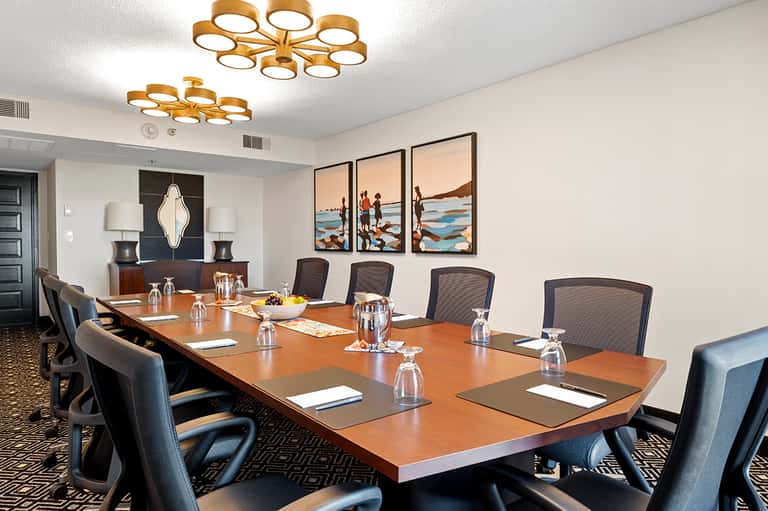 Modern conference room with long wooden table, black mesh chairs, and colorful beach artwork