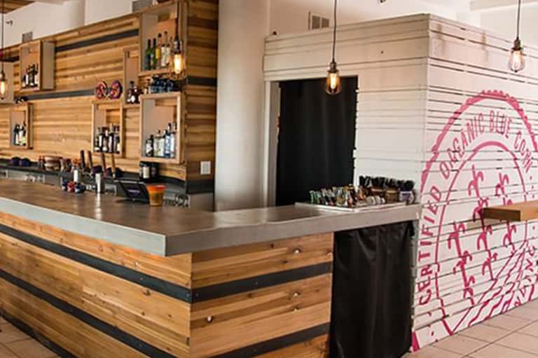 Contemporary bar interior with wooden slat walls, pendant lighting, counter seating, and pink neon wall art.
