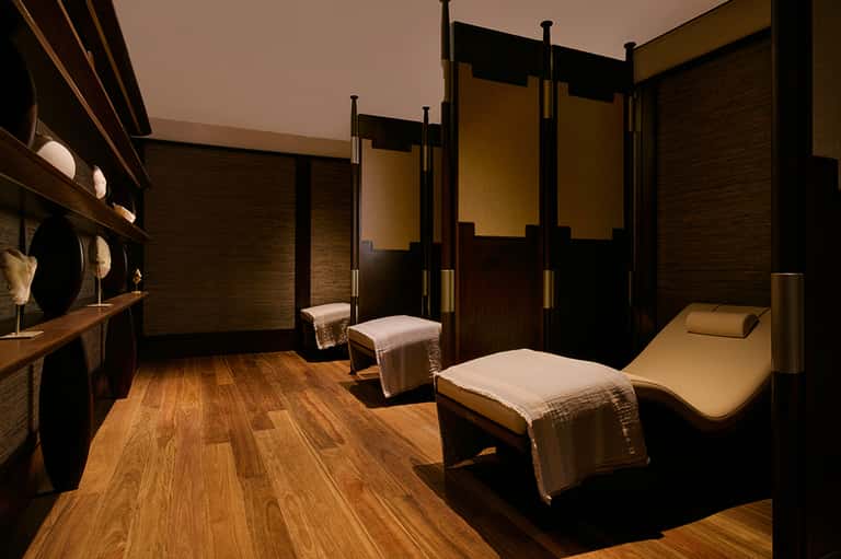 Luxury spa treatment room with wooden furnishings, massage beds, and warm amber and black interior design.