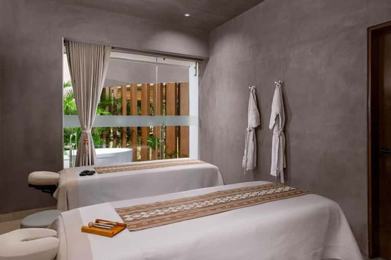 Spa treatment room with massage bed, wooden accents, natural light, and towel racks