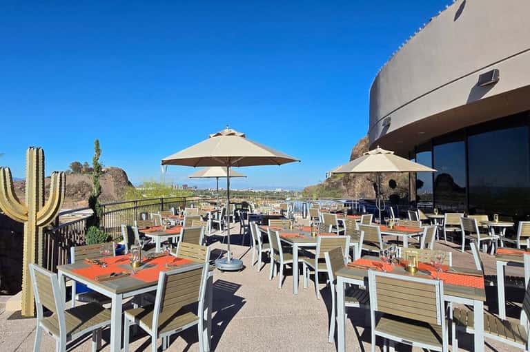 Outdoor dining terrace with tables, chairs, umbrellas, cacti, and scenic valley view