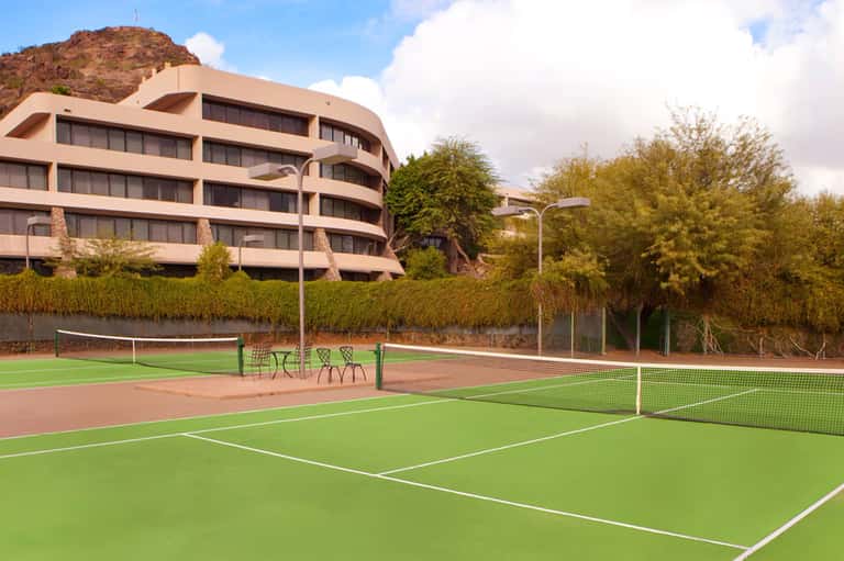 Modern curved residential building with tennis courts and green playing surfaces in foreground
