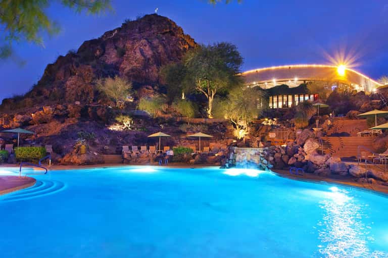 Illuminated resort pool with rocky landscape and mountain at dusk