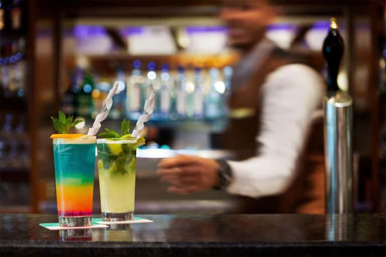 Colorful cocktails on bar counter with bartender in blurred background