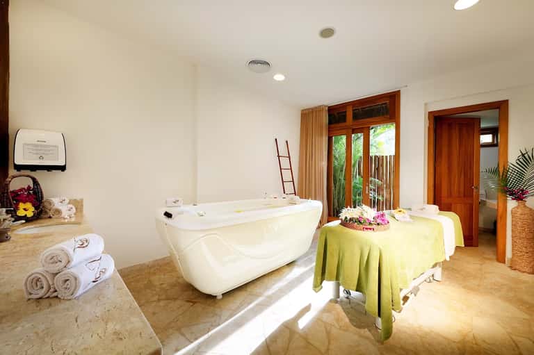 Spa treatment room with soaking tub, massage table, and tropical flowers