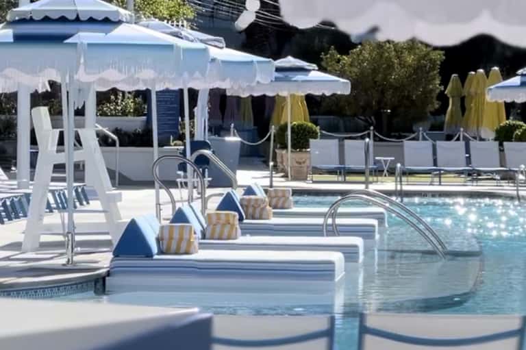 Luxurious resort pool with white cabanas, umbrellas, and lounge chairs on sunny day